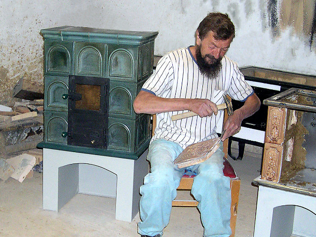 pp011-Pec (sálavá 3x2), kachlice „zelená kovová“ (po ravej ruke kachliara) Jozefa Pekaríka, ktorý osekáva kachlice na hnedý „hríb“