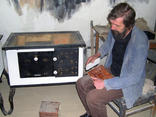 Kachliar Jozef Pekarík pri ručnom brúsení kachlíc, pri prenosnom šporáku omietanom